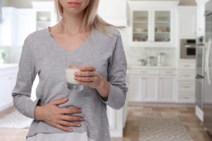 Dairy Intolerant person. Woman with stomach pain holding a glass of milk. Lactose intolerance, health care concept.